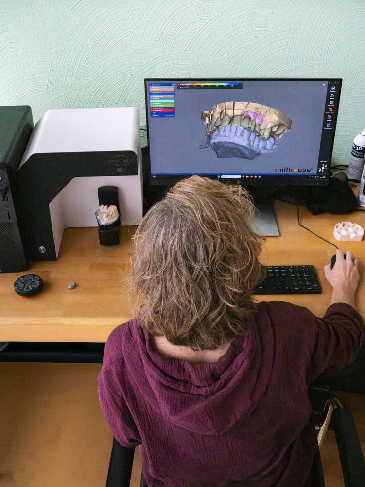 Zahntechnikerin konstruiert Zahnersatz am Bildschirm, links der Laborscanner